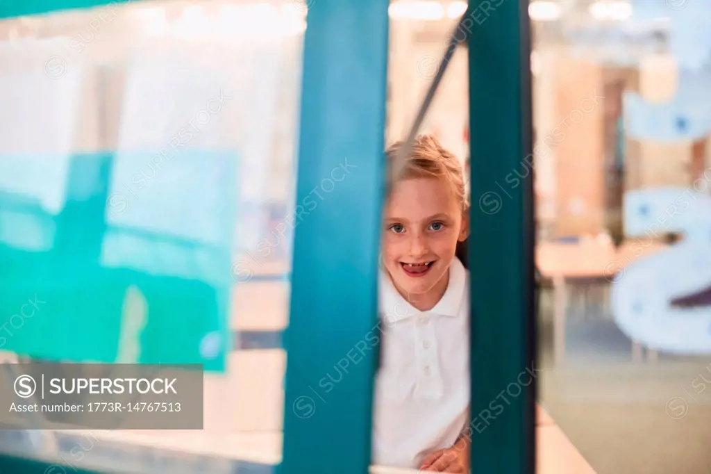 Portrait of schoolgirl looking through classroom window at primary school