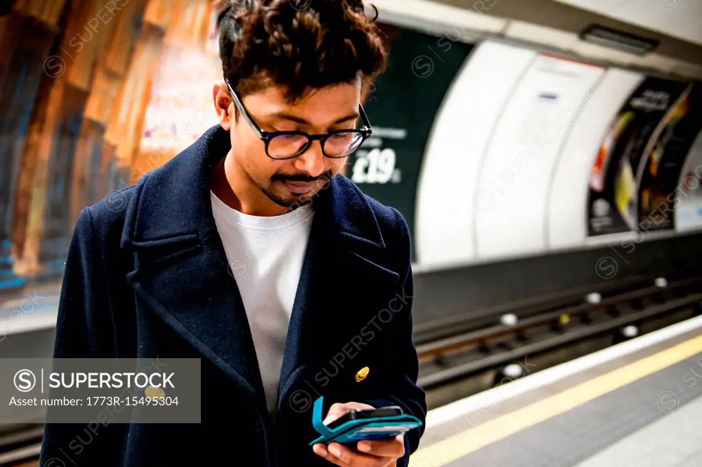 Businessman using smartphone on platform of subway station, London, UK