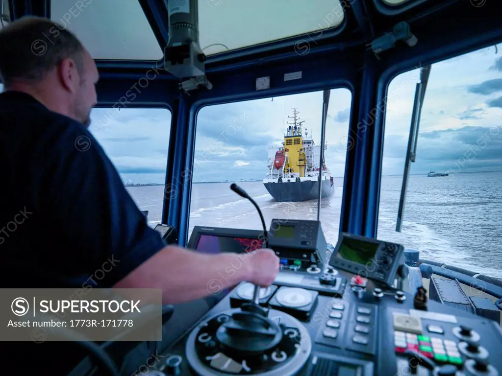 Worker driving tugboat in wheelhouse