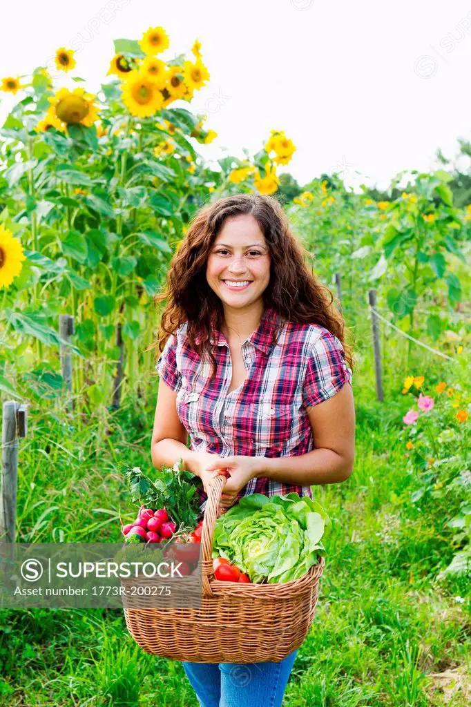 Portrait of young woman holding basket of fresh vegetables in allotment