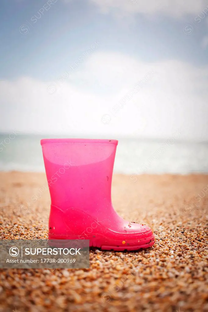Pink rubber boot standing on sand