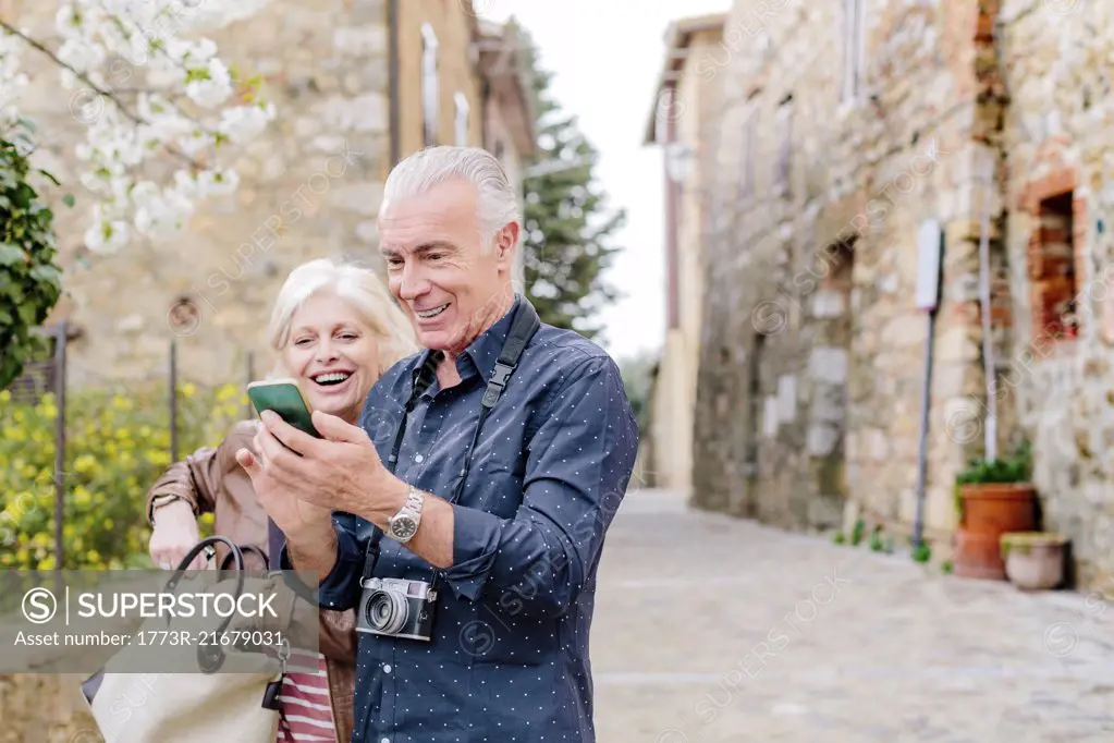 Tourist couple looking at smartphone on cobbled street, Siena, Tuscany, Italy