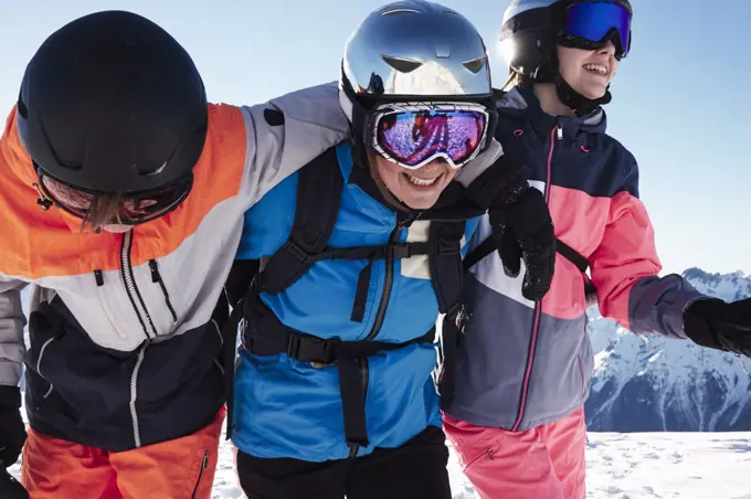 Skiers, mother with teenage son and daughter with arms around each other on snow covered mountain top,  Alpe-d'Huez, Rhone-Alpes, France