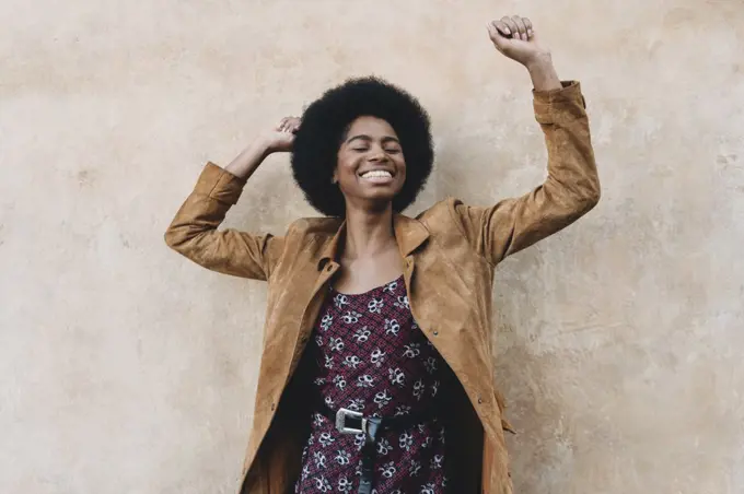 Young woman with afro hair feeling excited against stone wall