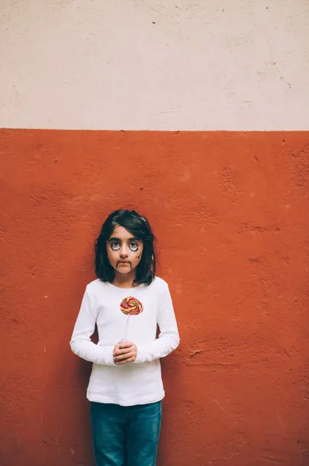 Girl with Halloween face paint, holding lollipop