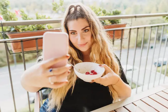 Young woman taking selfie with healthy breakfast bowl