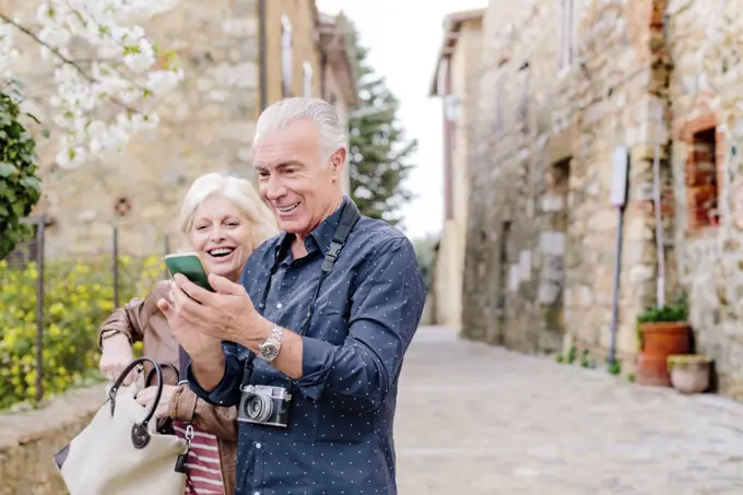 Tourist couple looking at smartphone on cobbled street, Siena, Tuscany, Italy