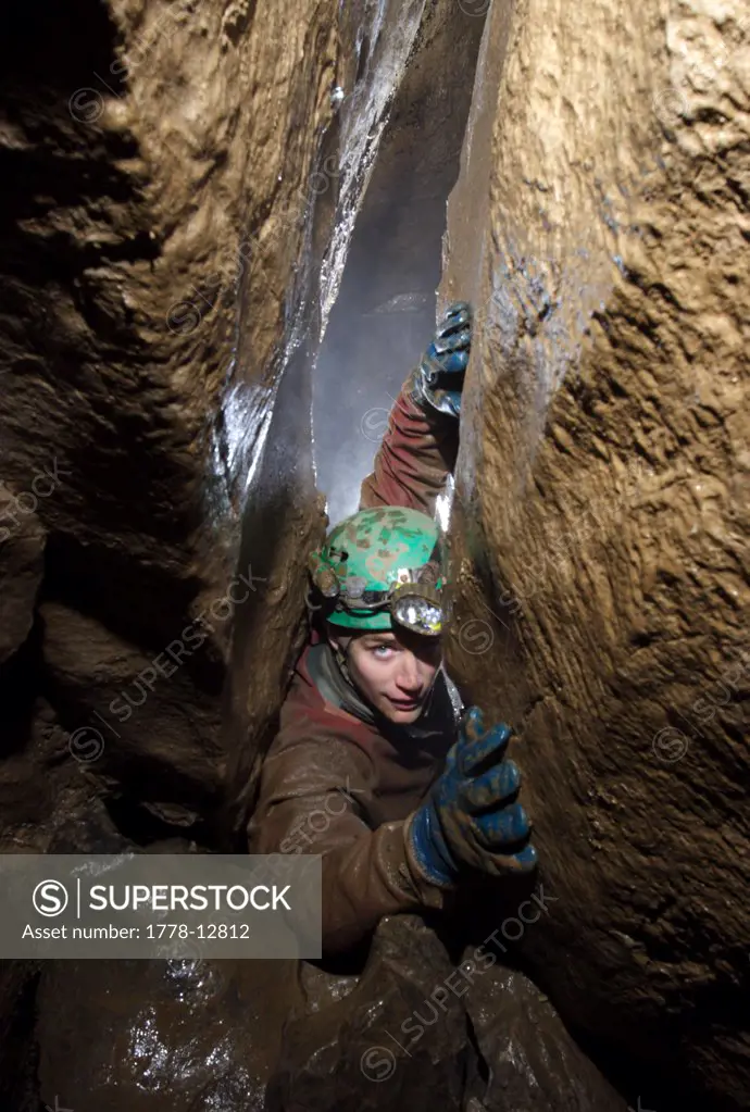 Cave explorer struggles to climb up a narrow section of cave passage underground in a cave called Streaks Pot in Derbyshire in E