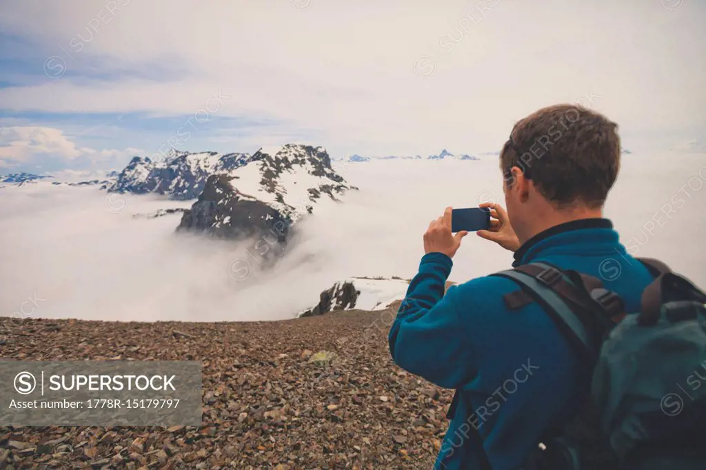 Rear view of hiker photographing view of mountains with smartphone, Cheam Mountain, Chilliwack, British Columbia, Canada