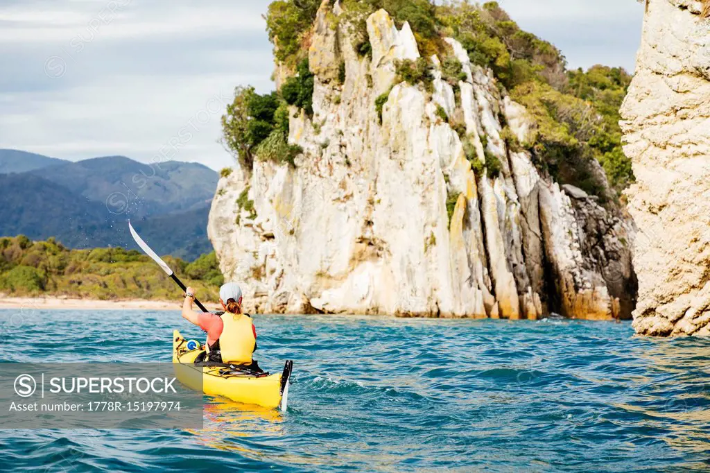 A woman is sea kayaking the coastline of Abel Tasman National Park