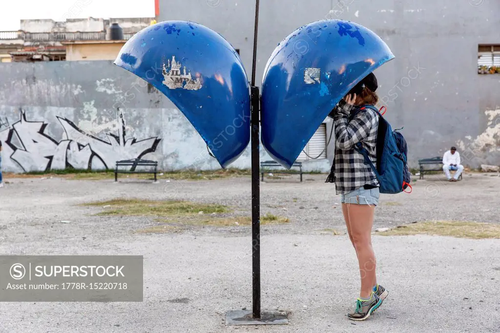 Side view of female tourist using payphone, Havana, Cuba