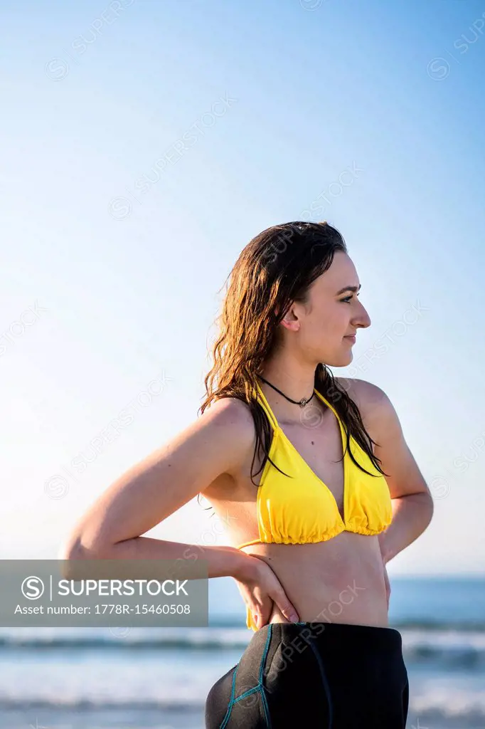 Side view shot of woman in yellow bikini on beach with arms akimbo