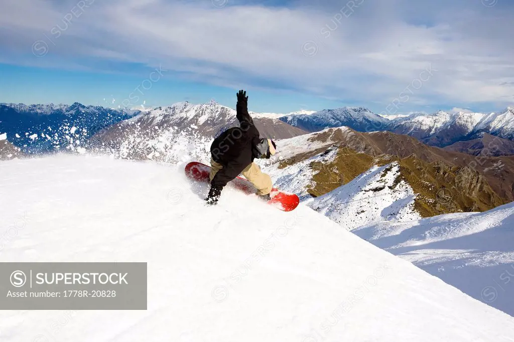 A male snowboarder blasts a heel side turn while snowboarding at Coronet Peak in Queenstown, New Zealand.