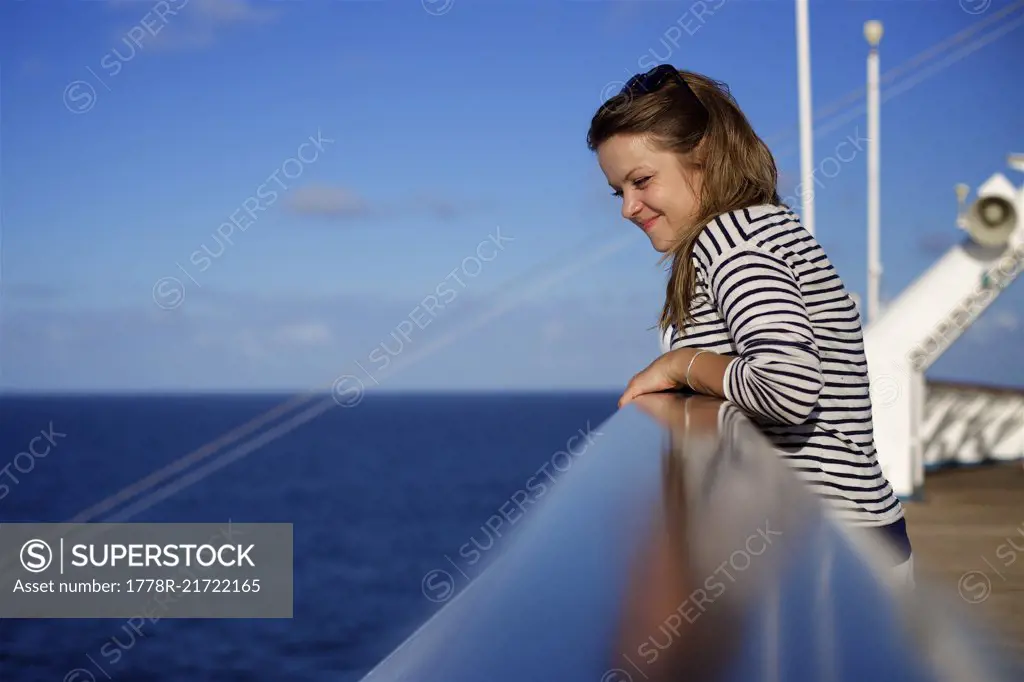 Side view of young woman leaning against railing on deck of cruise ship and looking into sea, Bahamas