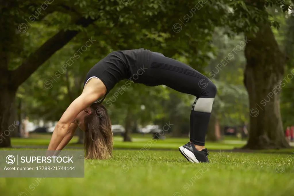 A woman does a back bend in the grass of the Boston Public Garden.