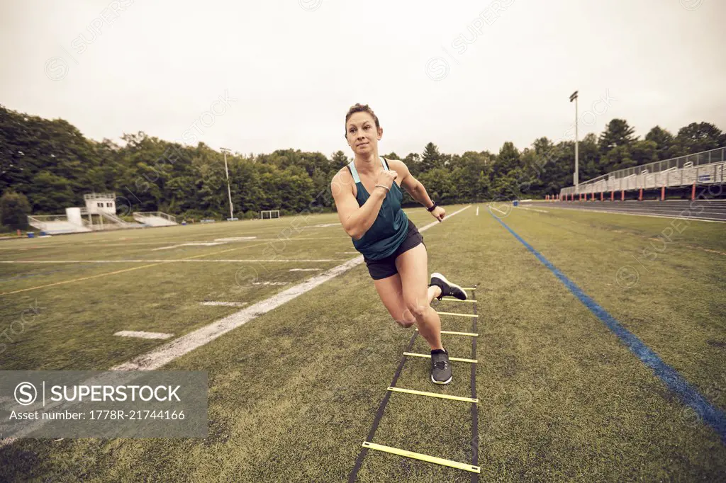 Front view of female athlete doing agility ladder exercises at athletic field, Lincoln, Massachusetts, USA