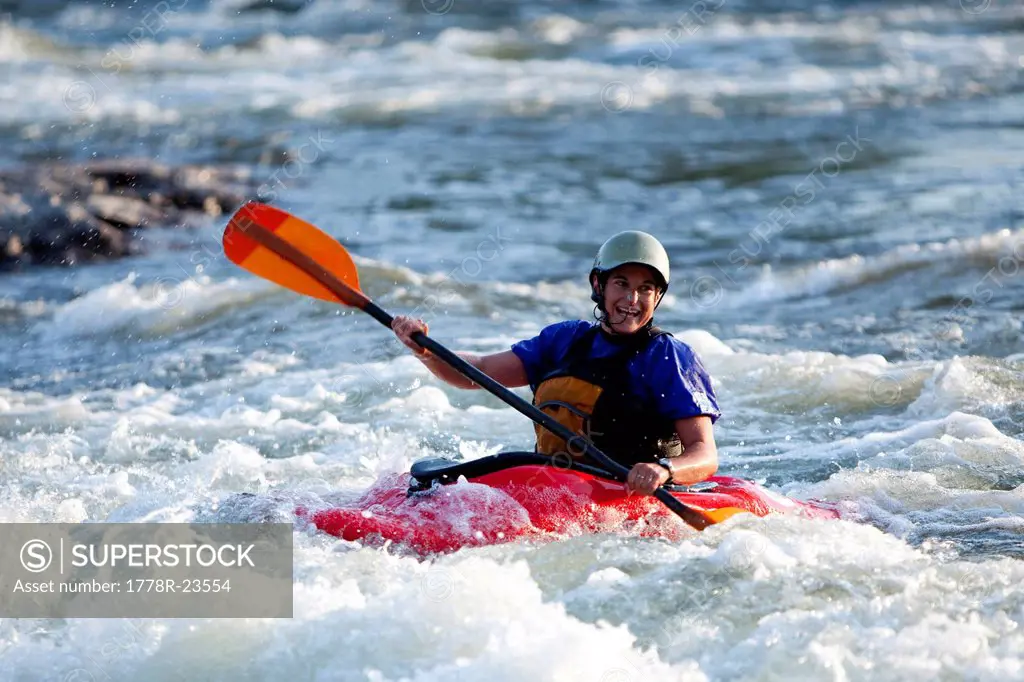 A female kayaker in a playboat paddles through rapids on the Clark Fork River, Missoula, Montana.