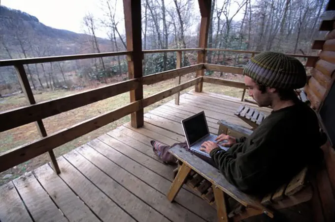 A man using his laptop on the porch of a wooden house near Jasper, Arkansas