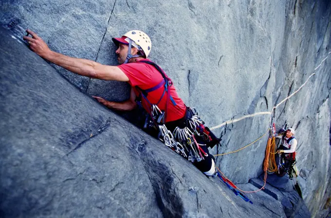 One man climbs while another man talks on his cell phone