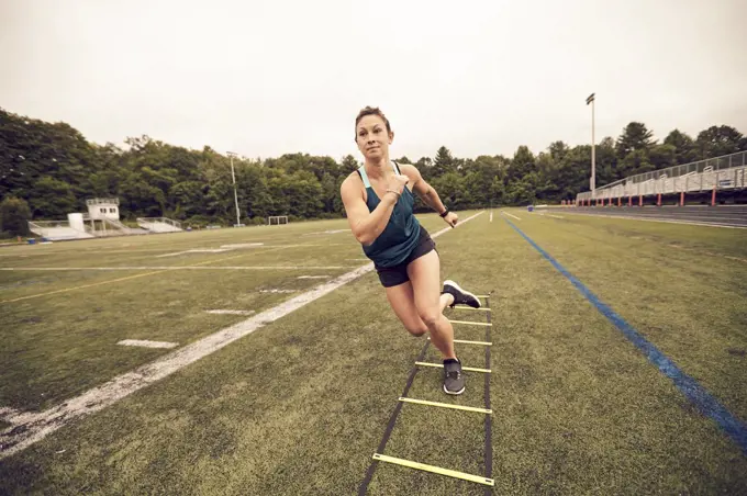 Front view of female athlete doing agility ladder exercises at athletic field, Lincoln, Massachusetts, USA