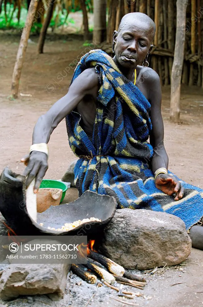 A Mursi tribal woman cooking 'tila' (a traditional dish made with maize or sorghum. Makki /South Omo / Southern Nations, Nationalities & People's Regi...