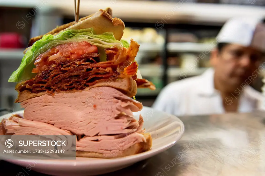 Large meat sandwich with chef in the background; New York City, New York, United States of America