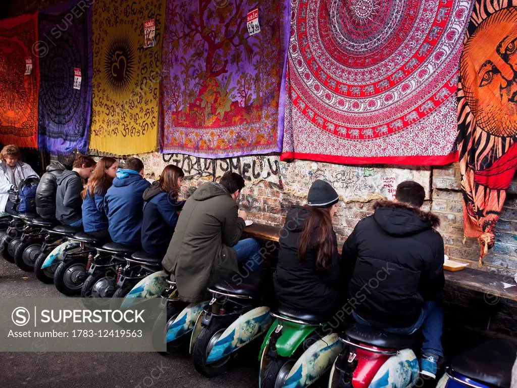 Al fresco dining seated on motor scooter stools, Camden Market; London, England