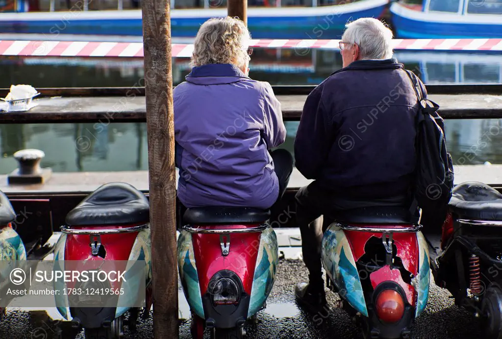 Senior couple sitting on Scooter stools at food stall, Camden market; London, England