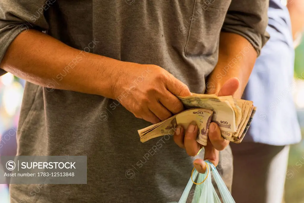 Man counting money in his hand with shopping bag at Old Market; Battambang, Cambodia