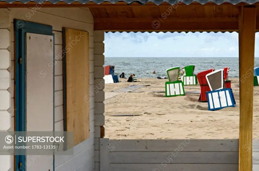 Covered beach chairs and beach hut on beach, Warnemunde, Germany.  Beach huts or strandkorb (German, literally Beach Basket) are special chairs designed to provide comfort and protection from sun, wind, rain, and sand on beaches. The strandkorb is said to have been invented in 1882 by German basket 