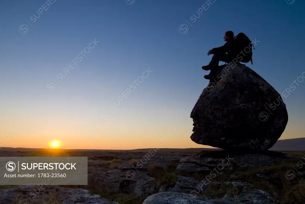 Hiker sitting on head-shaped boulder, Twisleton Scars near Ingleton, Yorkshire Dales National Park, North Yorkshire, England.