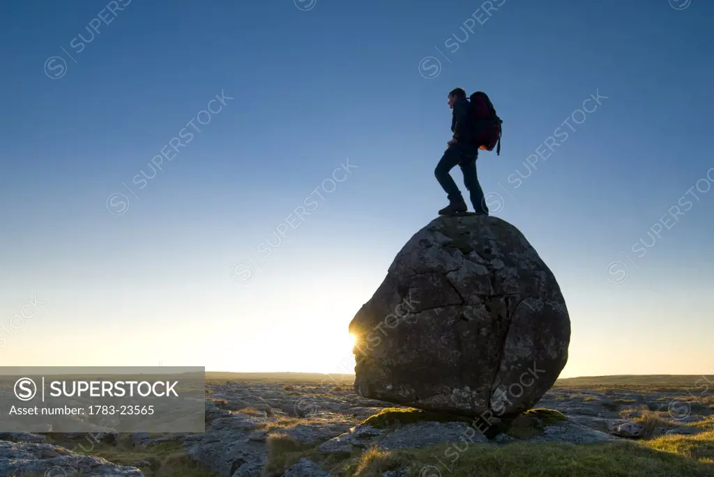 Hiker standing on head-shaped boulder, Twisleton Scars near Ingleton, Yorkshire Dales National Park, North Yorkshire, England.