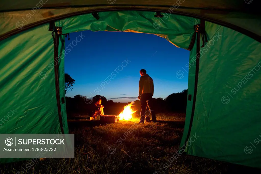 Couple camping with fire outside tent in field