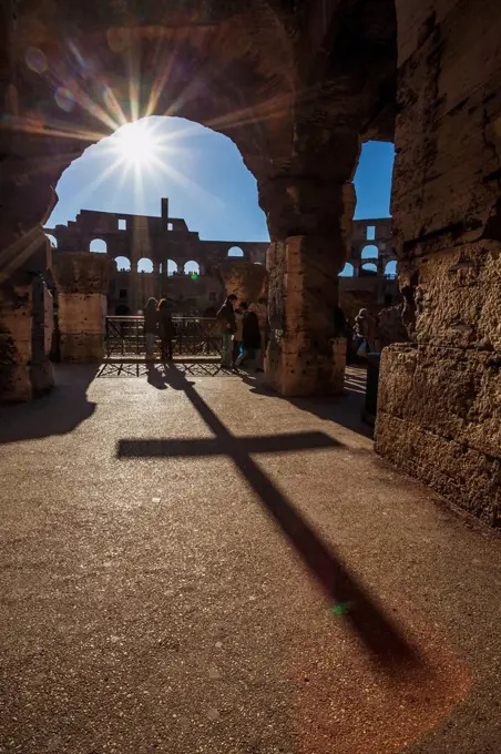 Sunburst through an archway at the Colosseum and a shadow of a cross; Rome, Italy