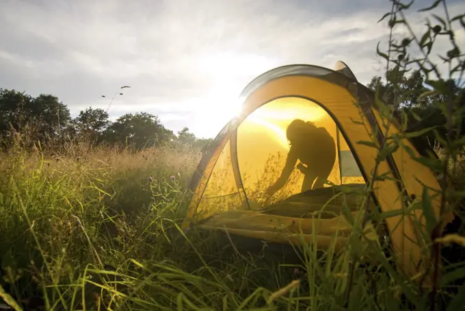 Person setting up tent in meadow, Groombridge, Kent, UK.