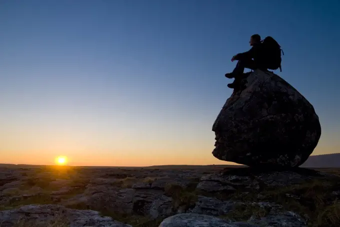 Hiker sitting on head-shaped boulder, Twisleton Scars near Ingleton, Yorkshire Dales National Park, North Yorkshire, England.