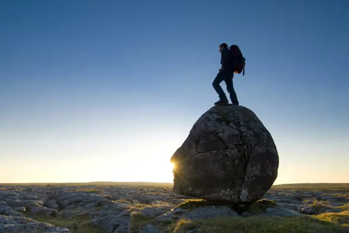 Hiker standing on head-shaped boulder, Twisleton Scars near Ingleton, Yorkshire Dales National Park, North Yorkshire, England.