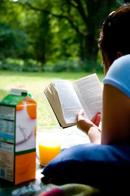 Girl reading a book and drinking orange juice, New Forest, Hollands Wood Campsite, Hampshire. 