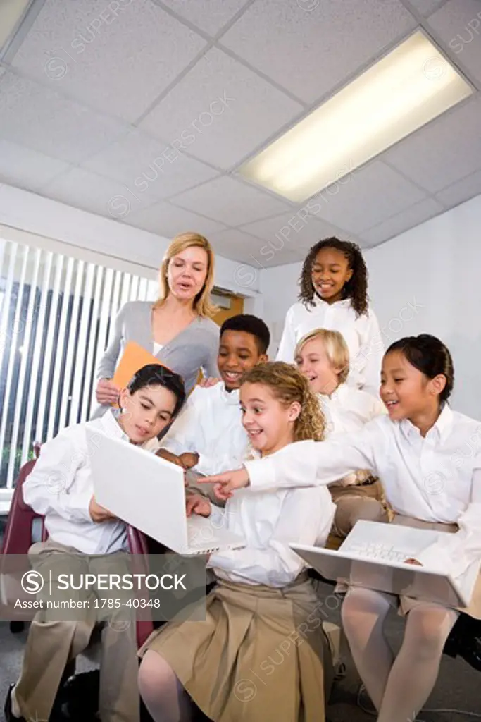 Diverse group of elementary students with teacher in class using laptops