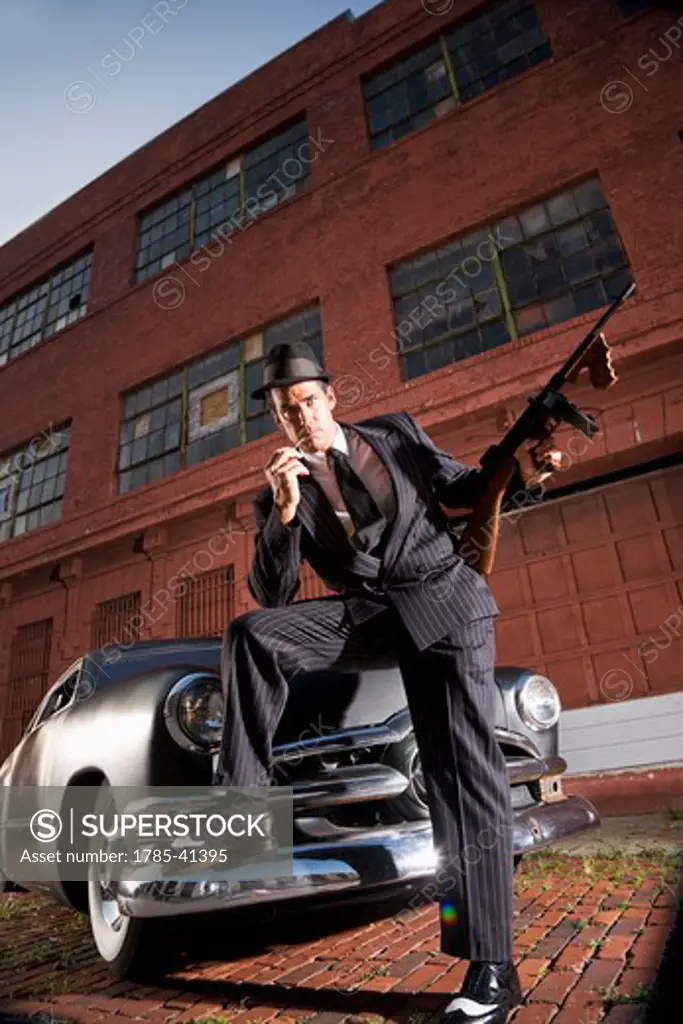 Gangster holding Tommy gun leaning on vintage car