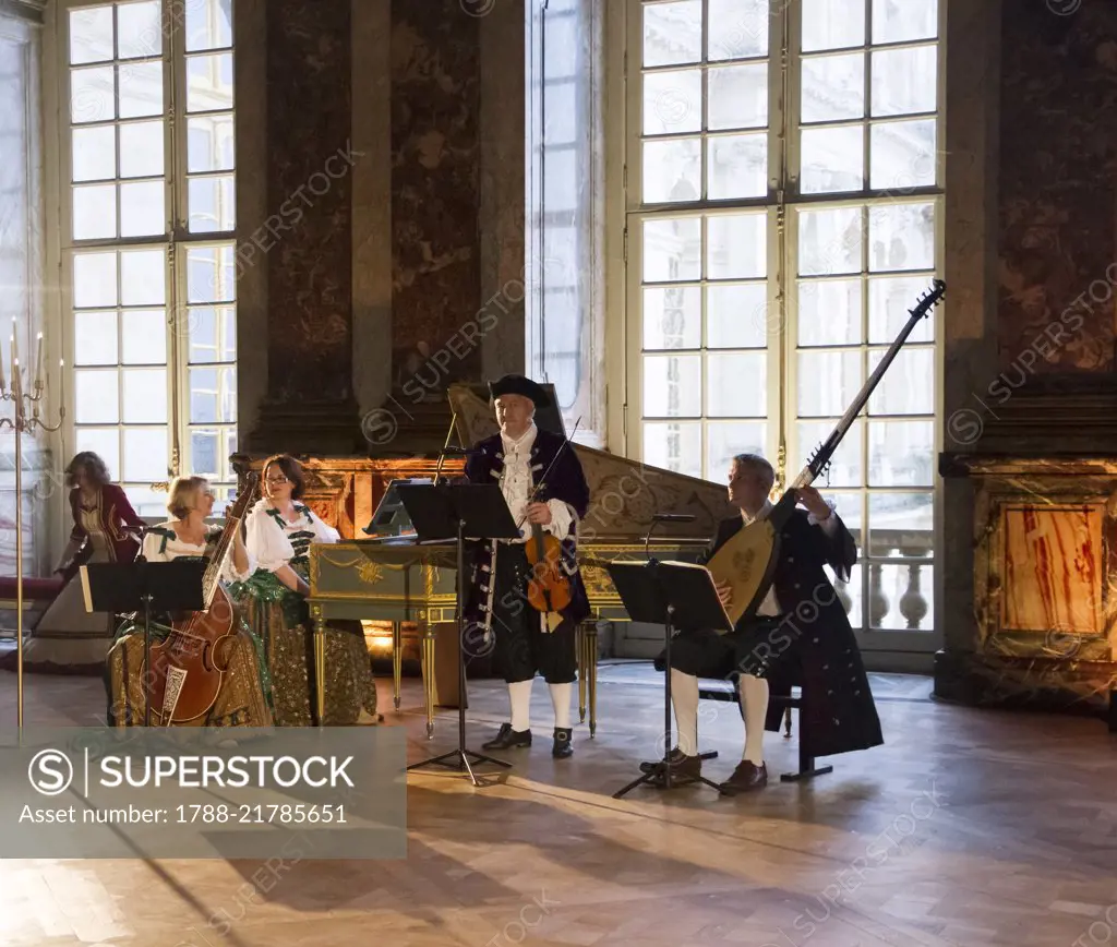 Musicians playing the viola, harpsichord, violin and theorbo, courtship party (Fete galante) with participants wearing clothes from the Louis XIV period, Palace of Versailles, France. Historical reenactment.