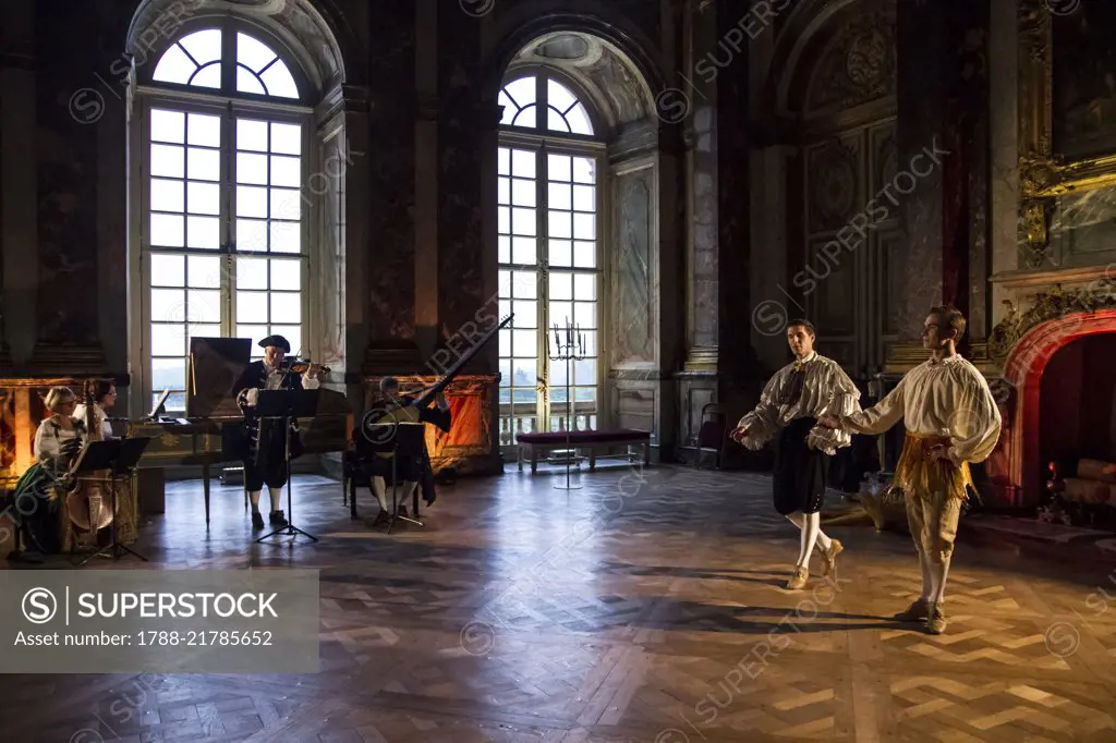 Musicians playing the viola, harpsichord, violin and theorbo; jesters and acrobats; courtship party (Fete galante) with participants wearing clothes from the Louis XIV period, Palace of Versailles, France. Historical reenactment.