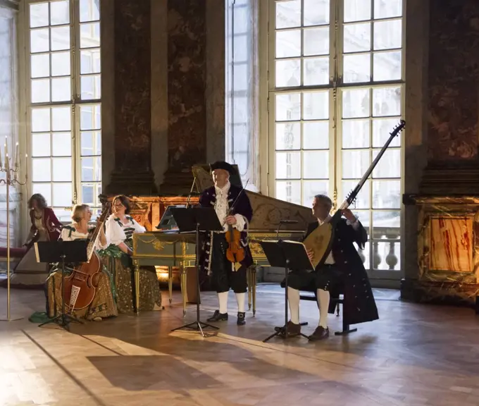 Musicians playing the viola, harpsichord, violin and theorbo, courtship party (Fete galante) with participants wearing clothes from the Louis XIV period, Palace of Versailles, France. Historical reenactment.