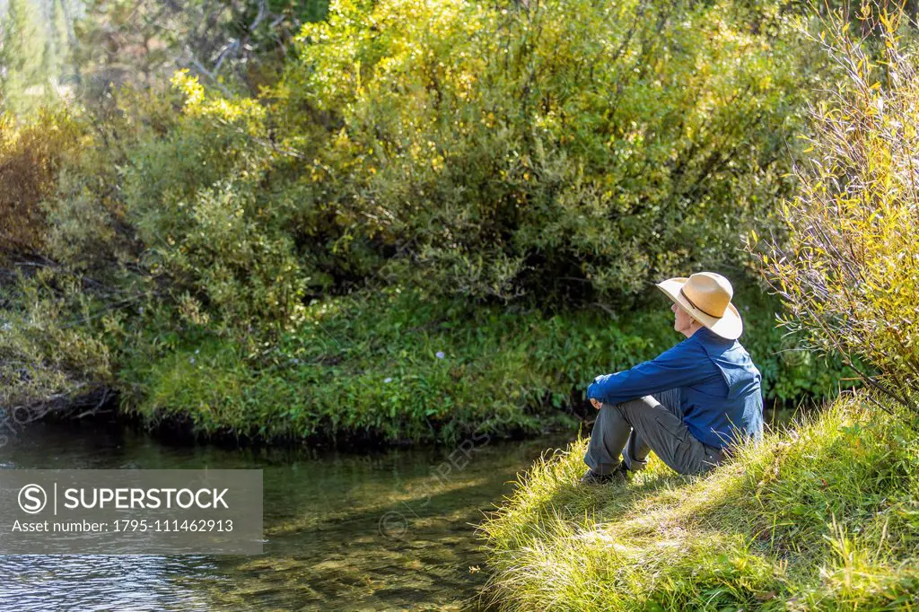 Man sitting on grass by steam in Stanley, Idaho, USA