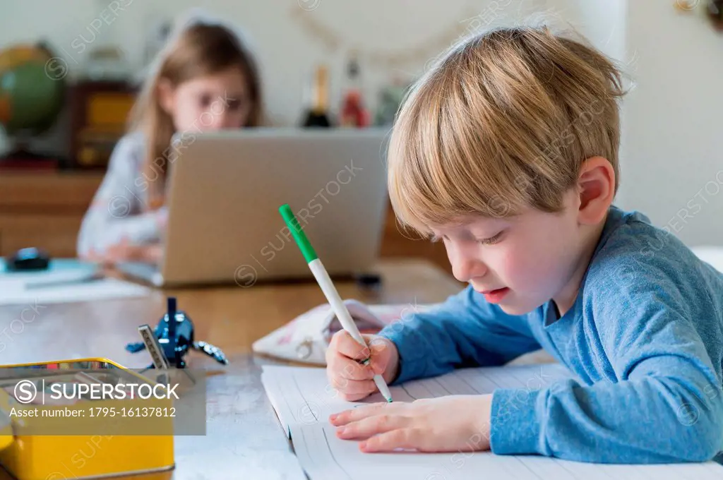 Boy (4-5) and girl (6-7) doing homework at table