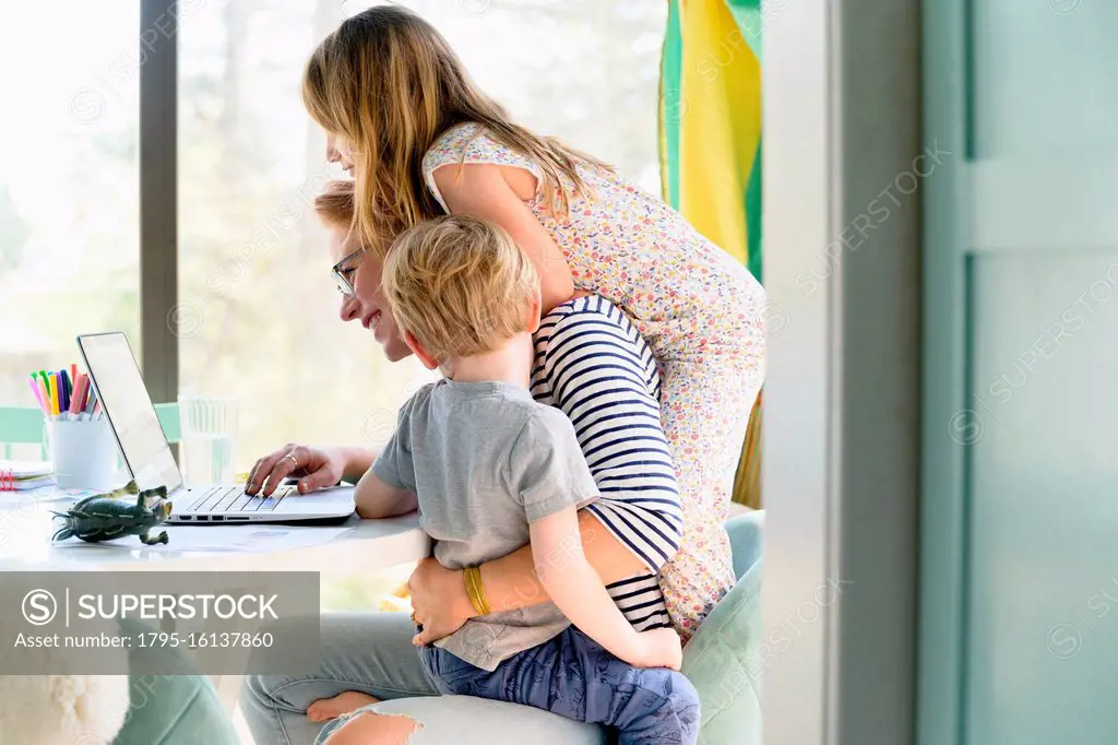 Children (4-5, 6-7) climbing on their mother while she works from home