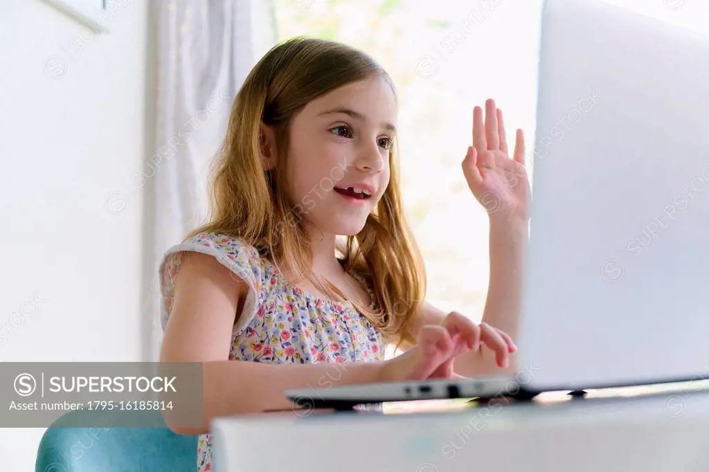 Girl (6-7) waving in front of laptop