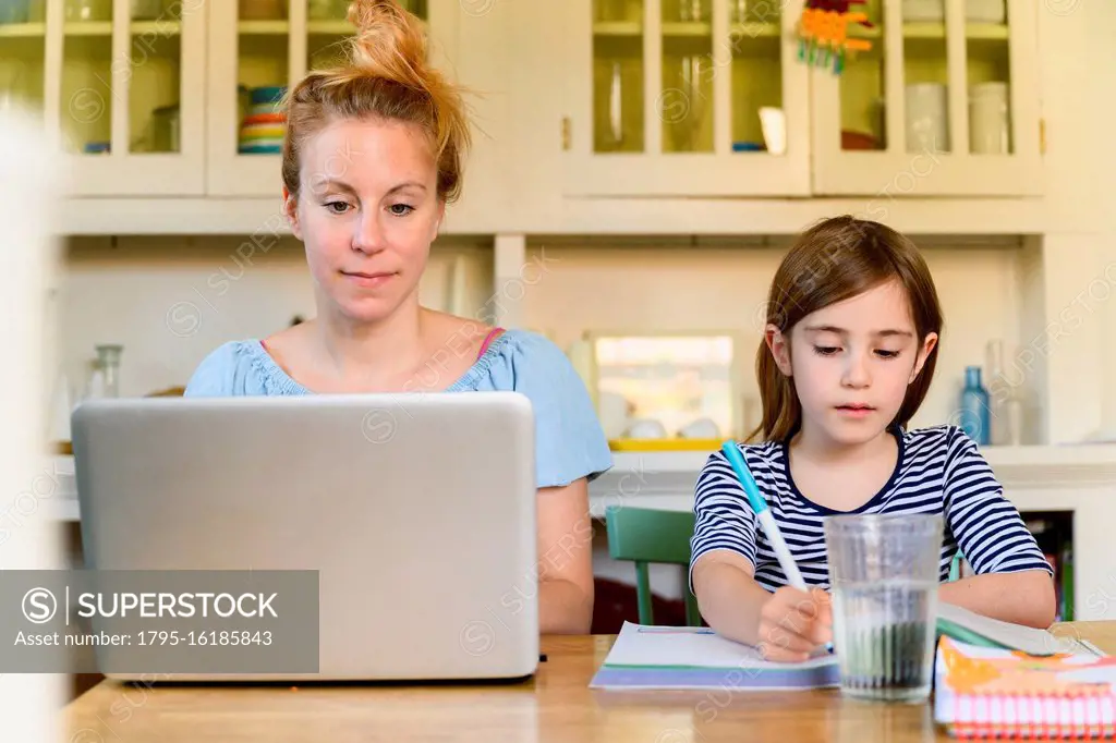 Woman working on laptop and girl (6-7) doing homework