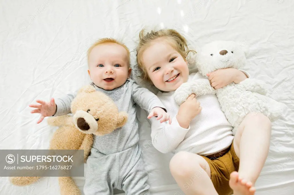 Portrait of siblings lying on bed with their teddy bears