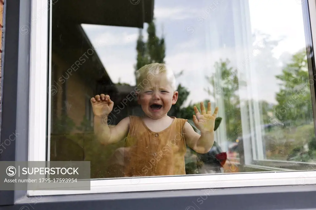 Baby boy (18-23 months) standing behind window and crying